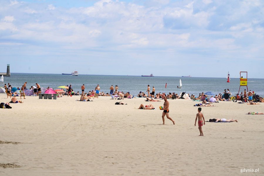 Plaża, ludzie i morze. W oddali stojące statki cargo. 