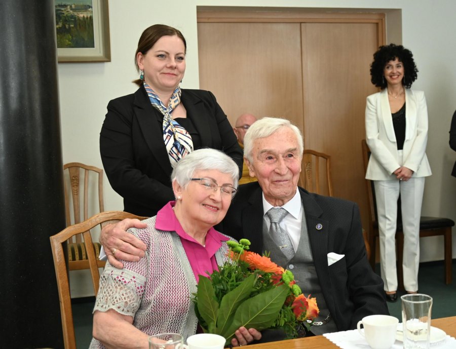 Para senior&oacute;w na krzesłach za nimi stoi kobieta w ciemnej marynarce