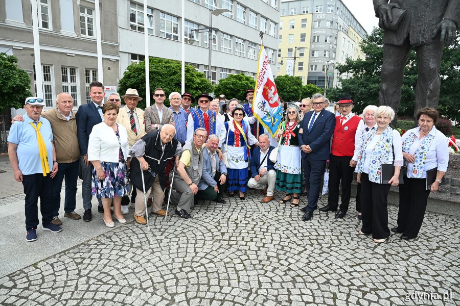Grupa ludzi pod pomnikiem w ludowych strojach