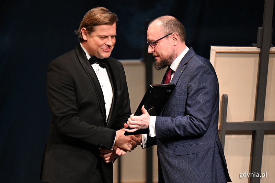 Mariusz Bzdęga - dyrektor zarządzający ds. kultury i aktywności mieszkańców wręcza Nagrodę Prezydent Miasta Gdyni z okazji Międzynarodowego Dnia Teatru  aktorowi Teatru Miejskiego Szymonowi Sędrowskiemu 