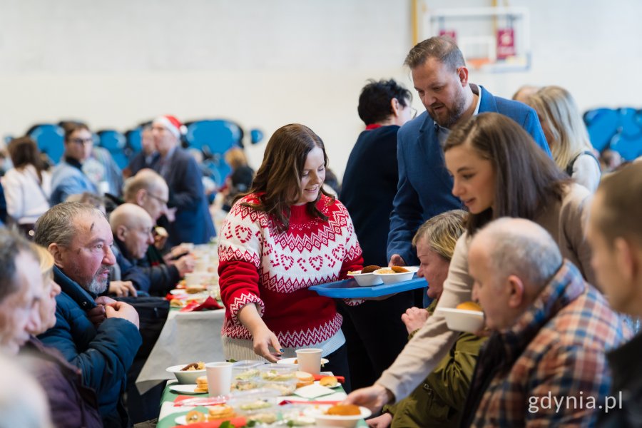 Prezydent Gdyni Aleksandra Kosiorek i radny Łukasz Strzałkowski roznoszący świąteczne potrawy gościom wigilii dla samotnych i potrzebujących 
