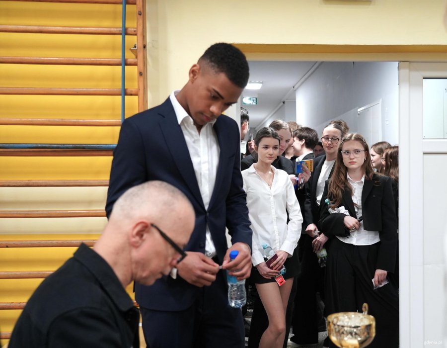 Chłopak w garniturze, za nim tłum młodych ludzi