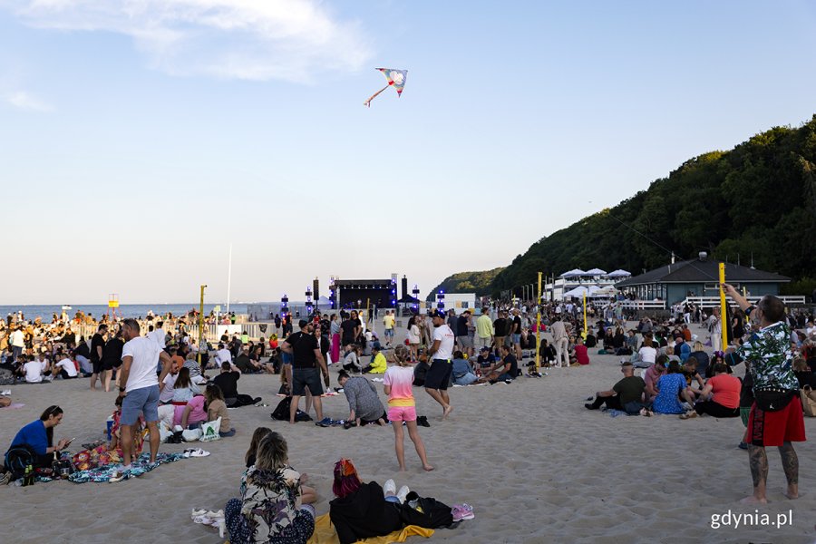 Ludzie siedzą wieczorem na plaży, w tle scena.