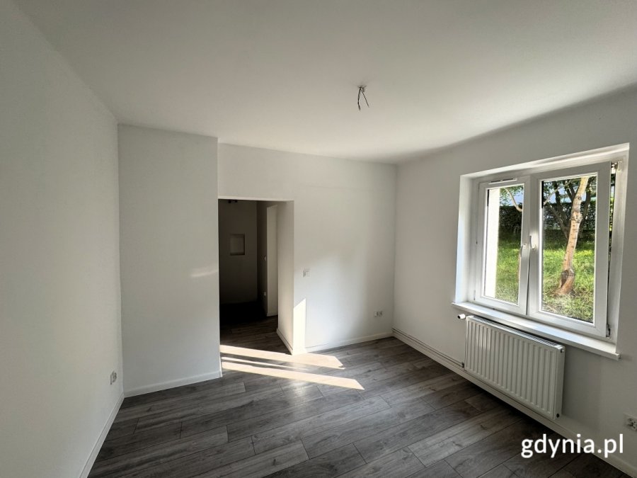 Na zdjęciu widać salon mieszkania, w dalszym planie widoczne są również okna.