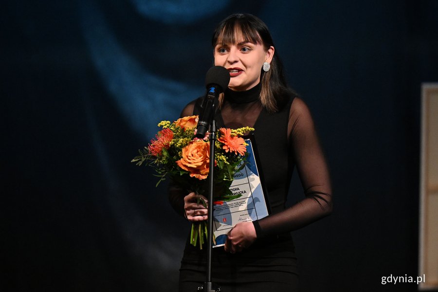 Krzysztofa Gomółka-Pawlicka z Teatru Gdynia Główna w eleganckim stroju po odebraniu Nagrody Prezydent Miasta Gdyni z okazji Międzynarodowego Dnia Teatru. W rękach trzyma kwiaty oraz dyplom 