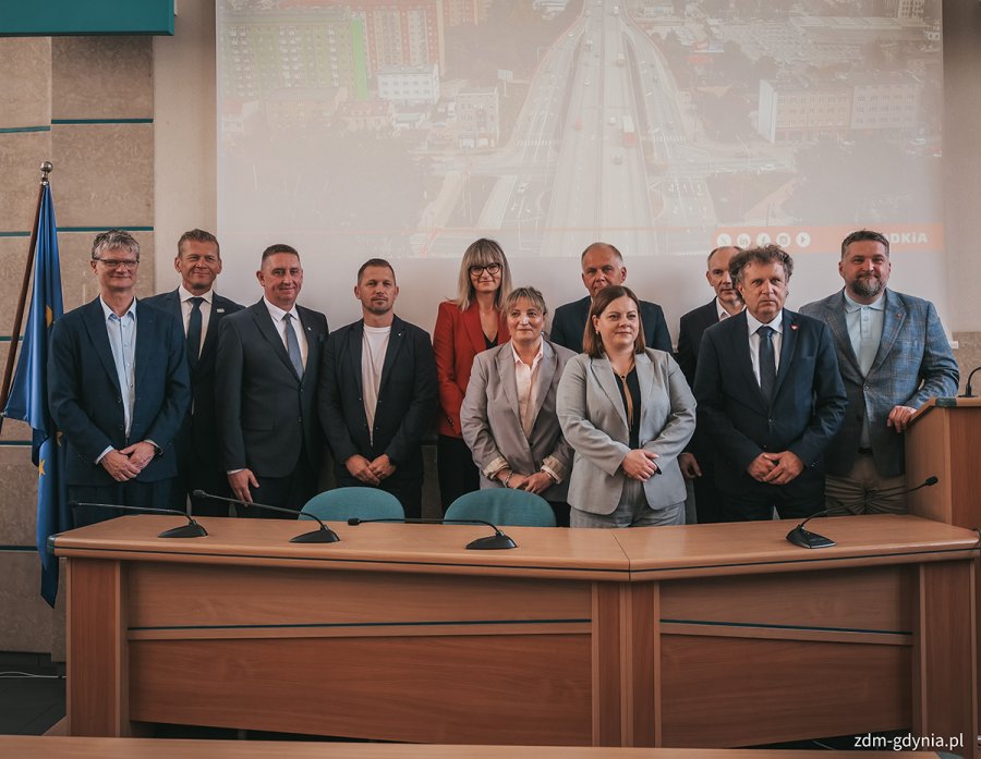 Wsp&oacute;lne zdjęcie podczas konferencji prasowej 26 maja. Od lewej: wiceprezydent Gdyni Rafał Geremek, dyrektor Zarządu Dr&oacute;g Miejskich w Gdyni Michał Felon, dyrektor oddziału GDDKiA w Gdańsku Karol Markowski, pracownicy Zarządu Dr&oacute;g Miejskich, prezydent Gdyni Aleksandra Kosiorek, sekretarz stanu w Ministerstwie Funduszy i Polityki Regionalnej Jacek Karnowski oraz Przewodniczący Rady Miasta Gdyni Tadeusz Szemiot. Wszyscy stoją za stołem prezydialnym w sali obrad (fot. Marcin Mielewski/ Zarząd Dr&oacute;g Miejskich)