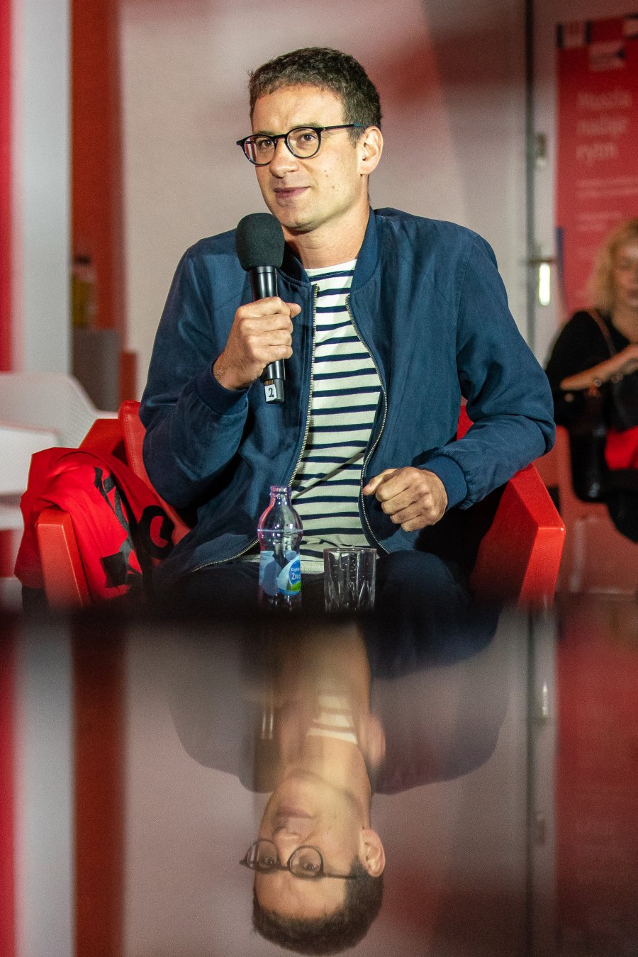 Mikołaj Łoziński - autor książki pt. "Stramer" - w koszulce w biało-czarne pasy i granatowej kurtce podczas spotkania na festiwalu "Miasto Słowa". W ręku trzyma mikrofon // fot. Anna Rezulak