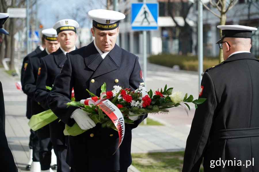Żołnierze w mundurach Marynarki Wojennej z wiązankami kwiatów