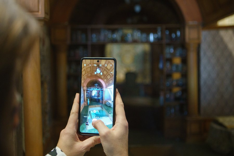 Na ekranie komórki widać korytarz w Muzeum Kart do Gry „Ulica Brydżowa”
