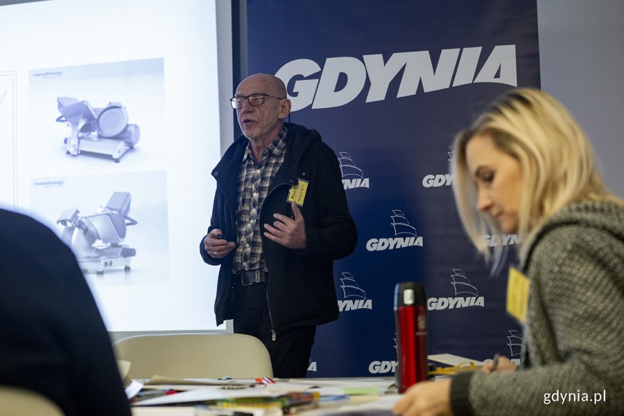 Przy ekranie stoi prof. Marek Adamczewski, na pierwszym planie siedzi przy stole uczestniczka warsztatów.