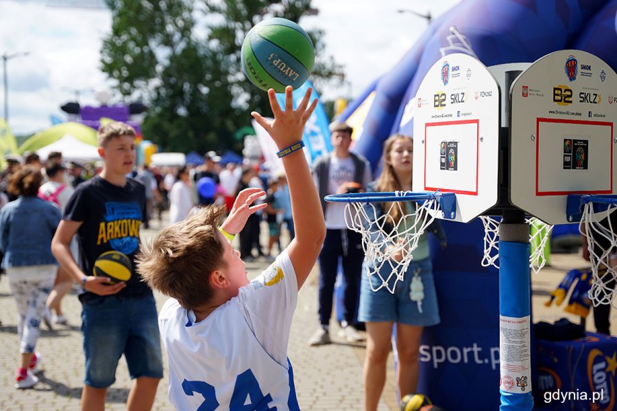 Młodzi ludzie z piłkami do kosza w rękach grają na torze sportowym w miasteczku stoczniowo-marynarskim podczas Dnia Marynarki Wojennej i Dnia Stoczniowca 