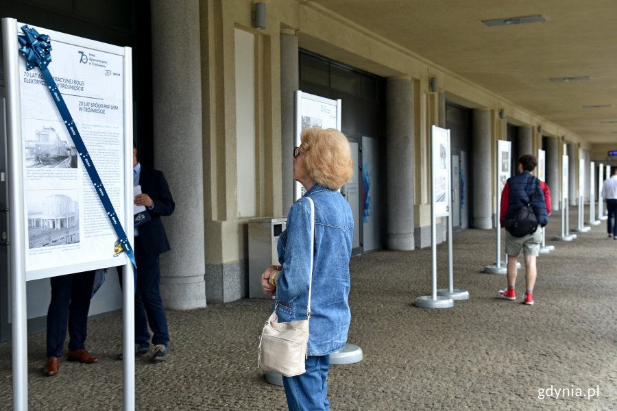 Kobieta i mężczyzna stoją przed tablicami ze zdjęciami. Oglądają wystawę z okazji 70-lecia Kolei Aglomeracyjnej w Trójmieście oraz 20-lecia spółki PKP SKM // fot. Magdalena Czernek