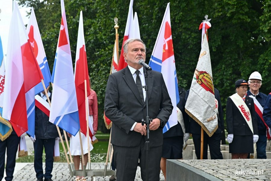 Wojciech Szczurek - prezydent Gdyni przemawiający podczas uroczystości z okazji 43. rocznicy strajków sierpniowych i podpisania porozumień sierpniowych. Za nim flagi Polski i Gdyni oraz poczty sztandarowe związkowców z NSZZ „Solidarność”  // fot. Magdalena Czernek