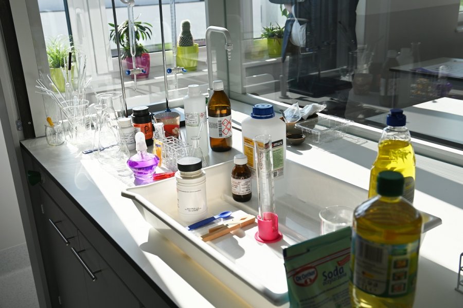 Na stoliku stoją szkła laboratoryjne z kolorowymi cieczami i inne instrumenty do nauki chemii