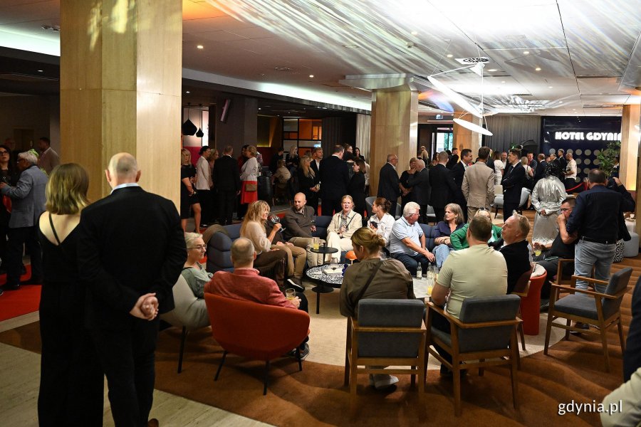 Kilkadziesiąt os&oacute;b, stojących i siedzących we foyer Hotelu Mercure Gdynia 