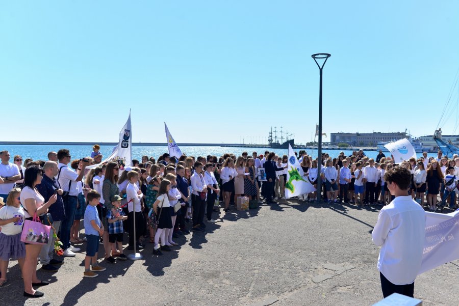 Goście wydarzenia stojący na marinie, za nimi może, w tle widać gdyńskie akwarium oraz żaglowiec