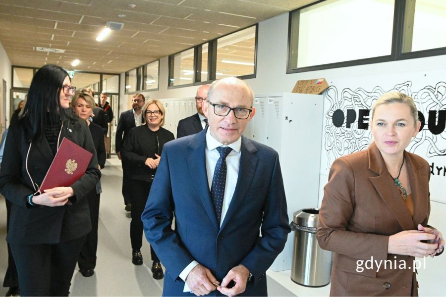 Grupa elegancko ubranych osób idąca po przestronnym korytarzu
