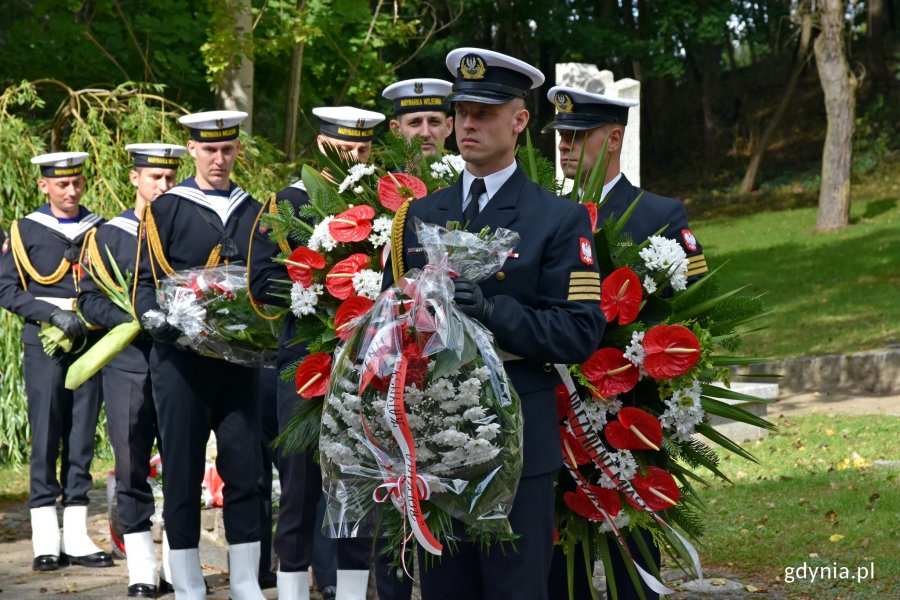 Żołnierze Marynarki Wojennej ustawieni w rzędzie, w rękach trzymają wieńce i wiązanki kwiatów // fot. Magdalena Czernek