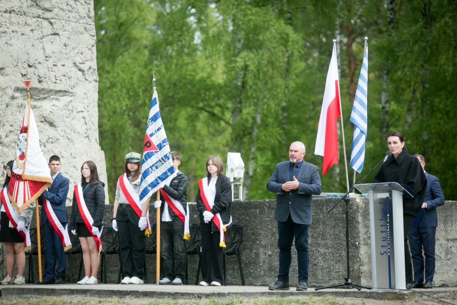 Beata Rutkiewicz, wojewoda pomorska, przemawiająca podczas uroczystości z okazji 80. rocznicy wyzwolenia obozu koncentracyjnego Stutthof. Obok mównicy stoją  poczty sztandarowe ze sztandarami