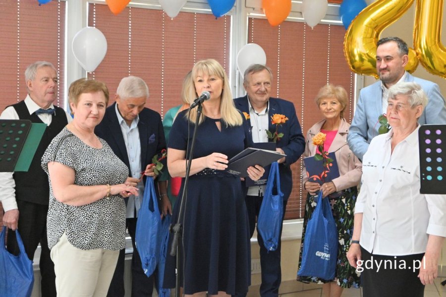 Grupa osób, w większości seniorów, stojąca w udekorowanej sali