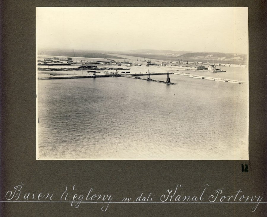 Fotografia czarno-biała naniesiona na kartę albumu „Foto-Elite” ze zdjęciami dokumentującymi gdyński port w 1929 roku. Przedstawia widok na basen Węglowy z nabrzeża Szwedzkiego. Widoczna budowa nabrzeża Duńskiego i Holenderskiego. W głębi, z prawej strony, mieści się budynek Kapitanatu Portu i magazyn tzw. „blaszak” na nabrzeżu Pilotowym. Pozytyw wykonany ze szklanego negatywu. Na karcie albumowej, pod zdjęciem odręcznie naniesiona informacja: „Basen Węglowy w dali Kanał Portowy” . Fotografia pochodzi z archiwum cyfrowego Muzeum Miasta Gdyni // fot. autor nieznany 