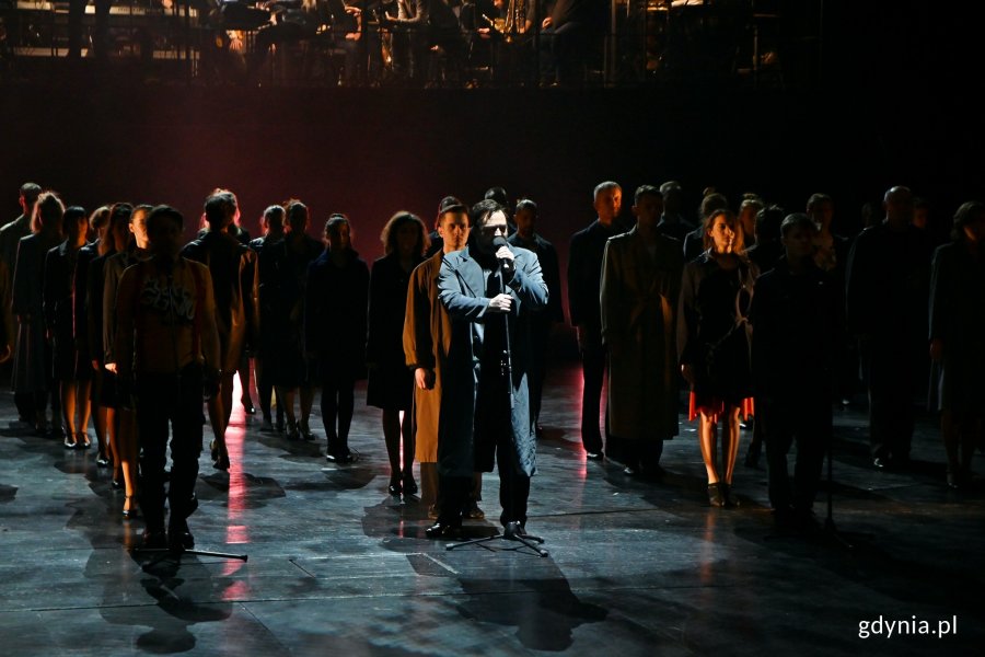 Zdjęcie z próby „Koncertu Sylwestrowego” w Teatrze Muzycznym w Gdyni. Scena zbiorowa. Rafał Ostrowski śpiewa oświetlony snopem światła // fot. Magdalena Czernek