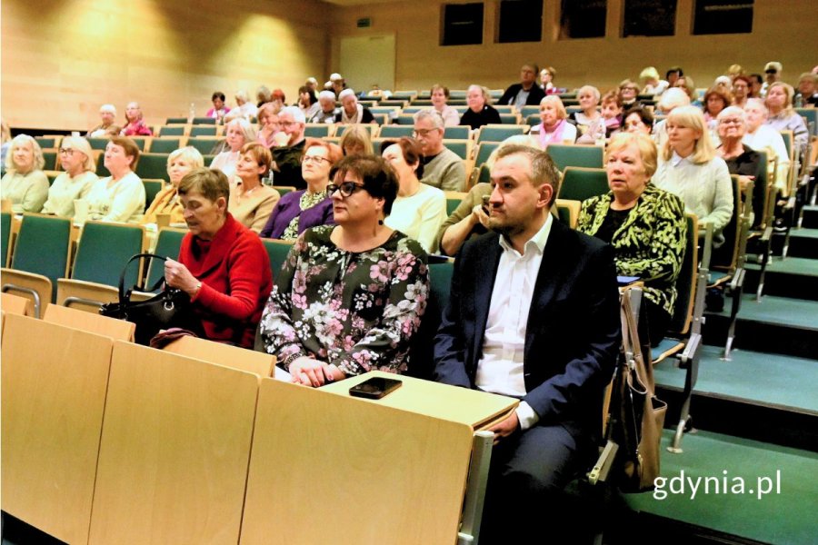 Wiele osób siedzących w rzędach krzeseł w auli