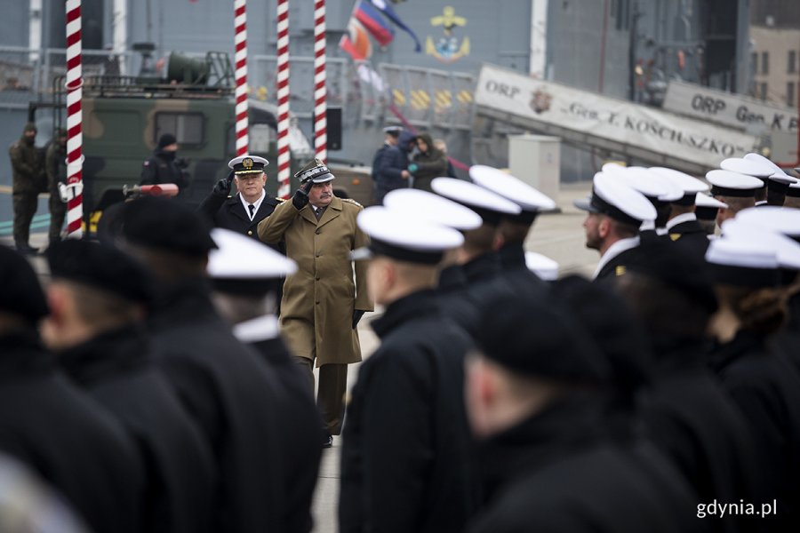 Dwóch żołnierzy maszeruje przed szeregami stojących marynarzy.