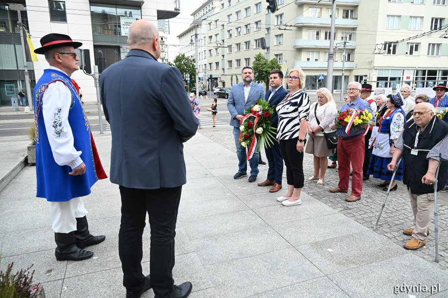 Osoby w ludowych strojach pod pomnikiem