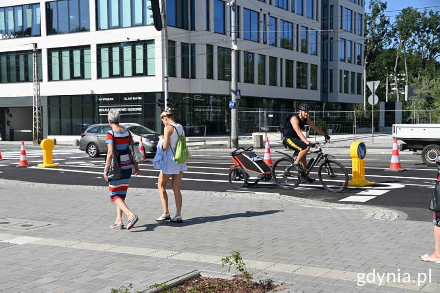 Rowerzysta z przyczepką na drodze rowerowej i dwie piesze na chodniku