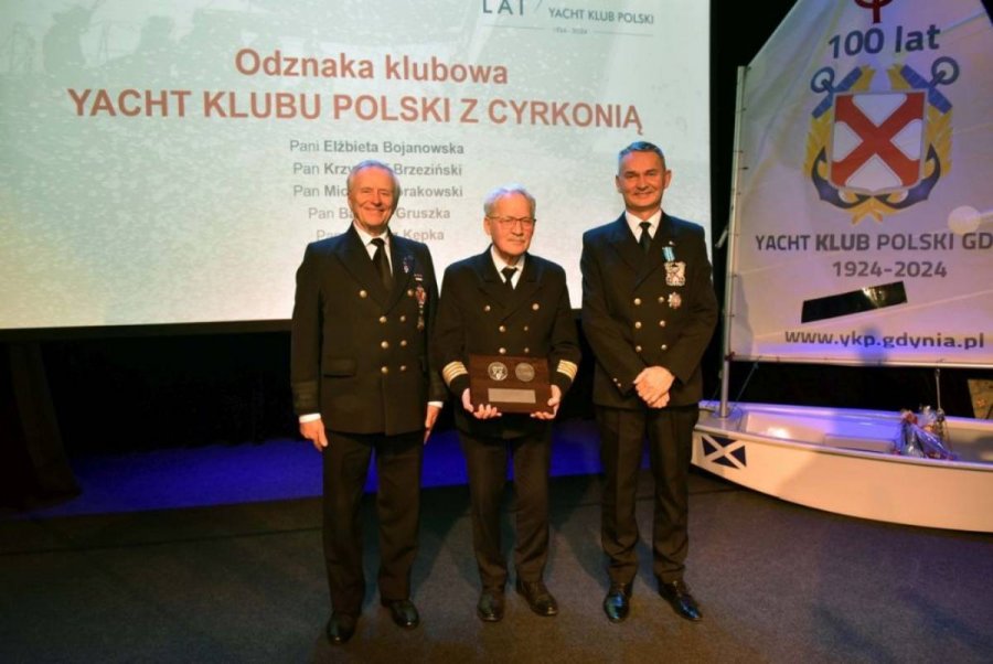 Grupa osób stojących na scenie i mających za plecami biały ekran