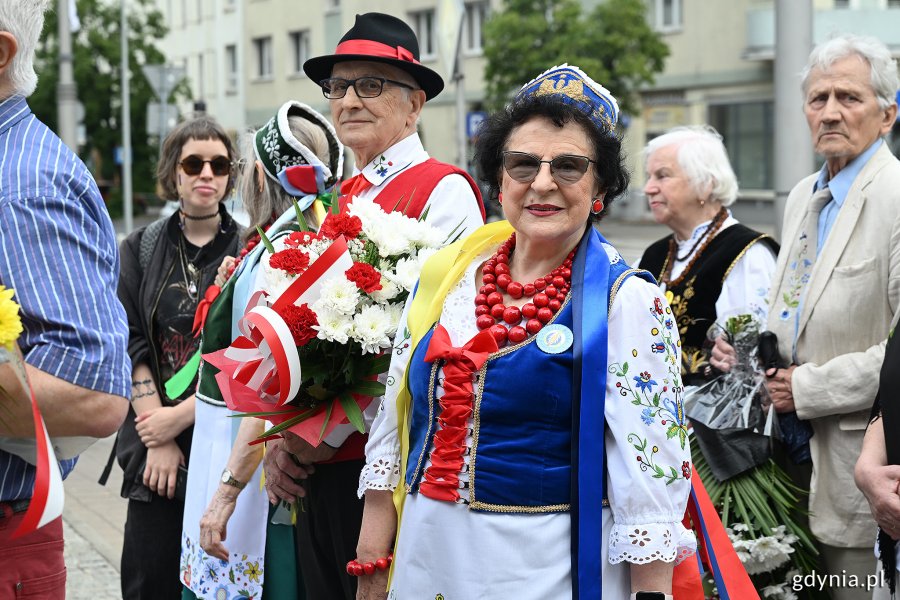 Osoby w ludowych strojach pod pomnikiem