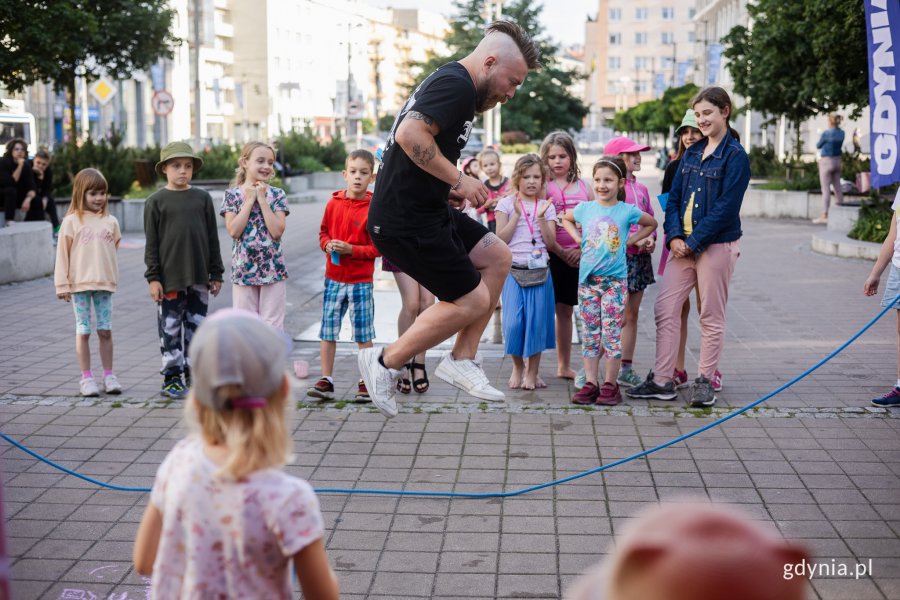Dzieci obserwują jak mężczyzna skacze przez linę.