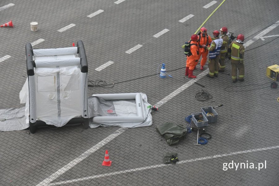 Strażacy stojący przy białej komorze do dekontaminacji