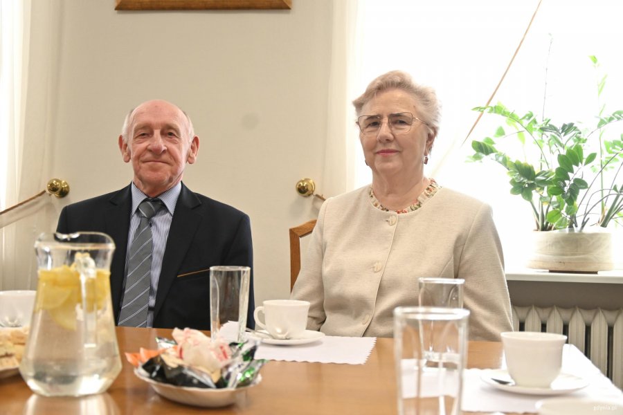 Mężczyzna w garniturze i kobieta w białym kostiumie przy stole