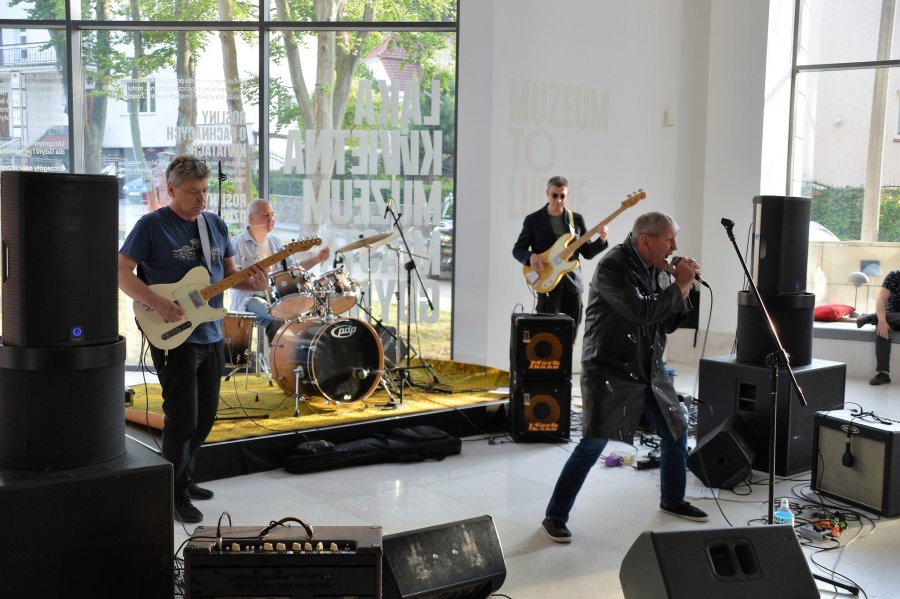 Na scenie Muzeum Miasta Gdyni występuje grupa Po Prostu: przy mikrofonie solista, obok dwóch basistów i perkusista 