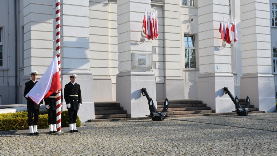 Poczet flagowy wciągający flagę RP na maszt przed budynkiem Komendy Portu Wojennego Gdynia podczas uroczystości z okazji 104. rocznicy sformowania tej jednostki 
