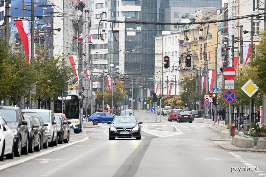 Biało-czerwone flagi na masztach i słupach ozdobią ulicę Świętojańską z okazji Święta Niepodległości. Flagi wiszą po bokach, w centrum zdjęcia ulica Świętojańska i jadące po niej samochody // fot. Michał Puszczewicz