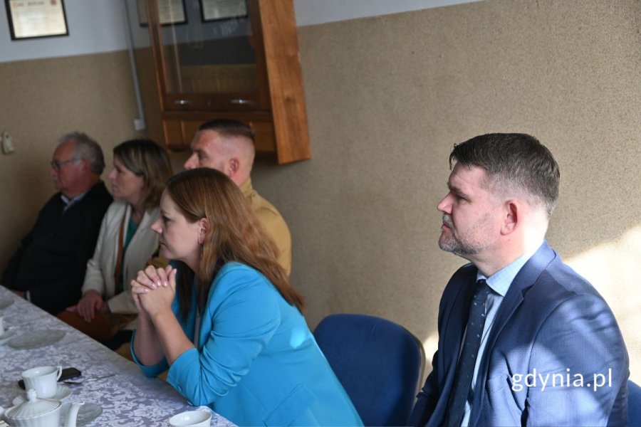 Mężczyźni i kobiety siedzący przy stole z białym obrusem i słuchający prelekcji