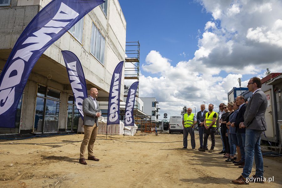 Plac budowy z lewej niewykończony budynek, po środku wiceprezydent Bartoszewicz, po prawej publiczność uroczystości