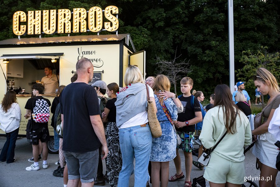 Ludzie stoją przed food truckiem.