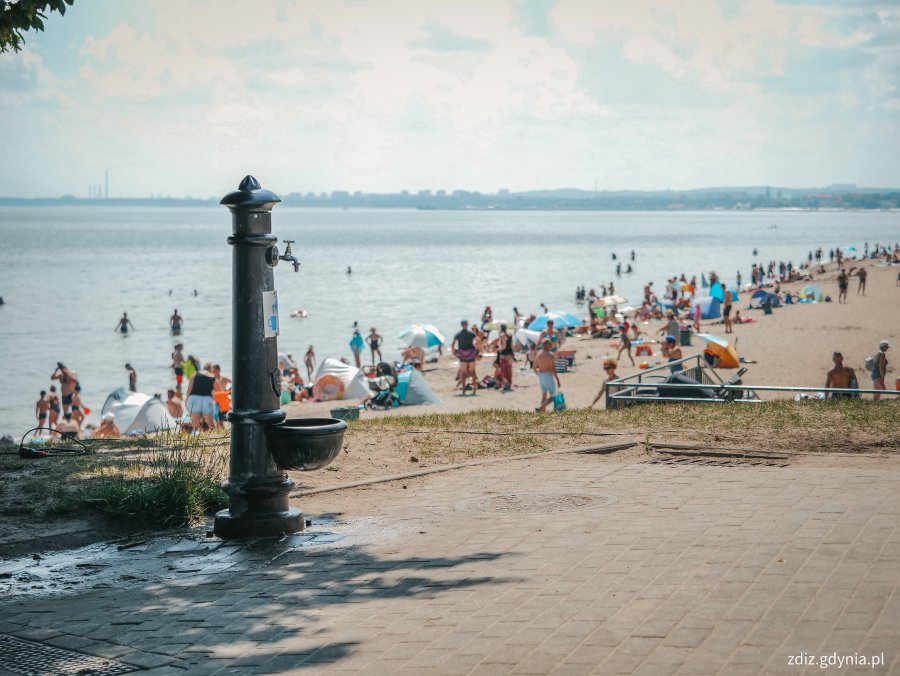 zdrój uliczny, w tle morze i plażujący ludzie