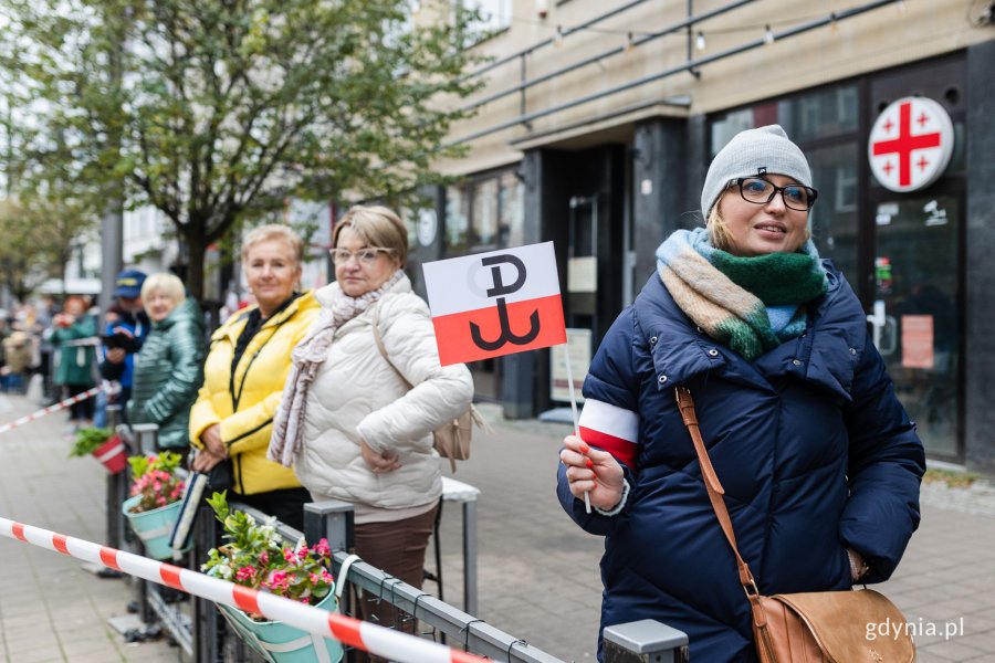 Osoby przyglądające się paradzie z okazji Narodowego Święta Niepodległości. Kobieta na pierwszym planie trzyma w ręku biało-czerwoną flagę z symbolem Polski Walczącej// fot. Karol Stańczak