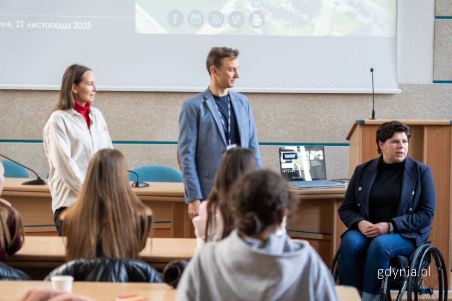 Kobieta na wzózku i mężczyna w garniturze przed grupą osób