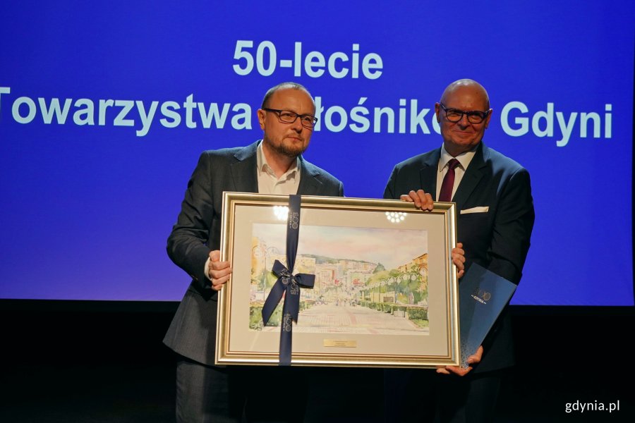 Mariusz Bzdęga &ndash; dyrektor zarządzający ds. kultury i aktywności mieszkańc&oacute;w przekazuje akwarelę Wojciechowi Kodłubańskiemu &ndash; prezesowi Towarzystwa Miłośnik&oacute;w Gdyni podczas uroczystości z okazji 50-lecia towarzystwa 