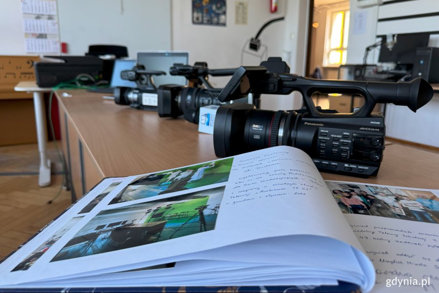 Sala ze stołami, na których stoją kamery video, na pierszym planie kronika, w dalszym planie radiowęzeł i drzwi wyjściowe z sali
