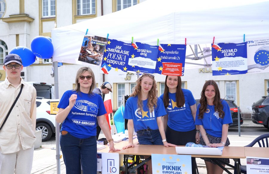 Nauczycielka i trzy uczennice w niebieskich koszulkach z emblematami UE