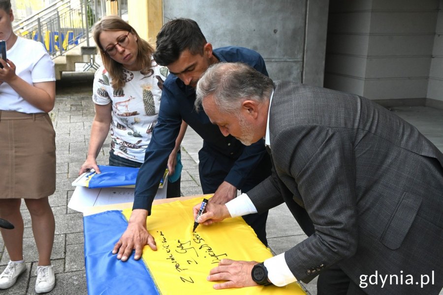 Prezydent Gdyni w towarzystwie Darii Balabai z Fundacji RC i Ihora Vashchuka podpisuje ukraińską flagę, która pojedzie do Chersonia