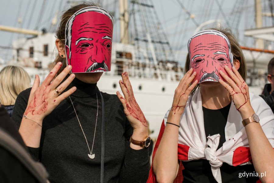 Uczestniczki manifestacji w maskach z podobizną Łukaszenki i sztuczną krwią na rękach. Dziewczyna po prawej ma przewiązaną na szyi flagę białoruską // fot. Karol Stańczak