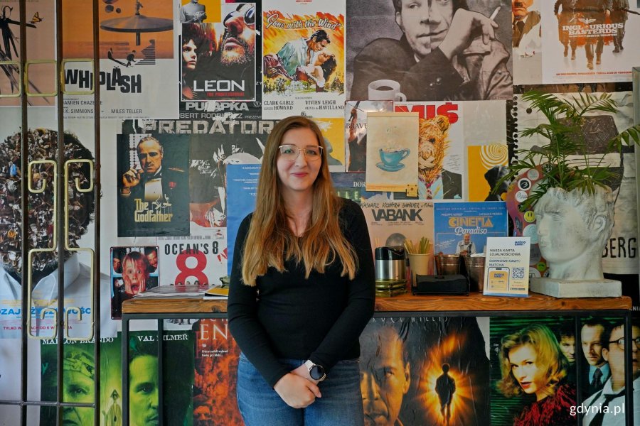 Pamela Dzi&oacute;bek &ndash; właścicielka kawiarni Może Kawy? na tle ściany z plakatami filmowymi 